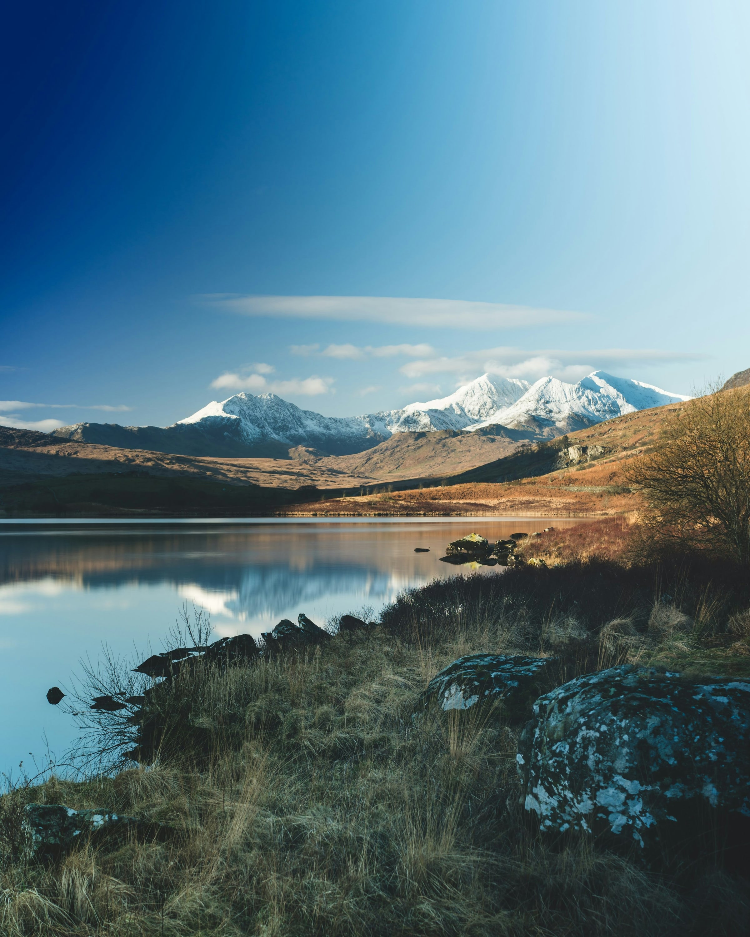 Snow-capped mountains reflected in a still lake under a clear blue sky